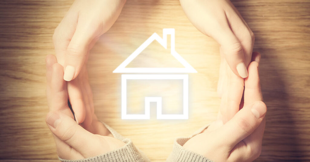Two hands encircle a glowing house icon