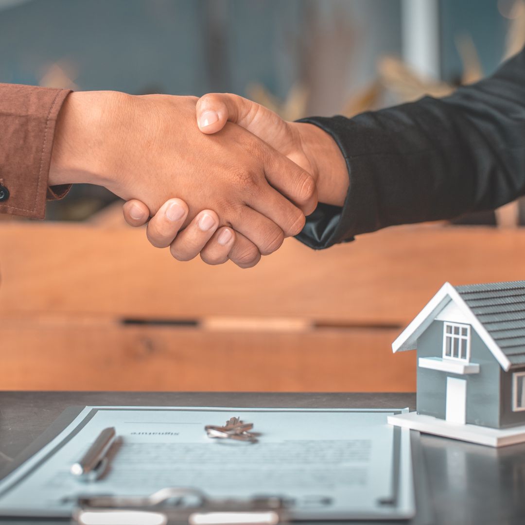 people shaking hands over paperwork and a toy house