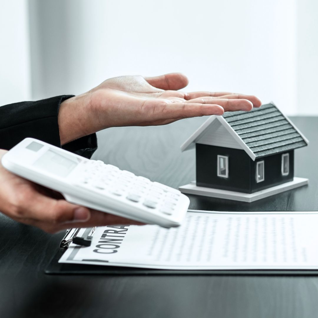 a business person holding out a calculator with paperwork and a toy home in the background