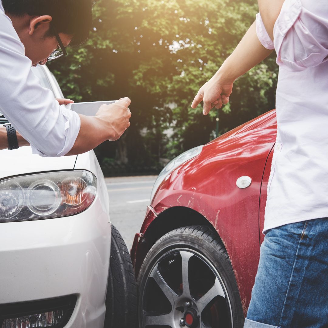 Man taking a photo of vehicle damage with his phone after a car accident