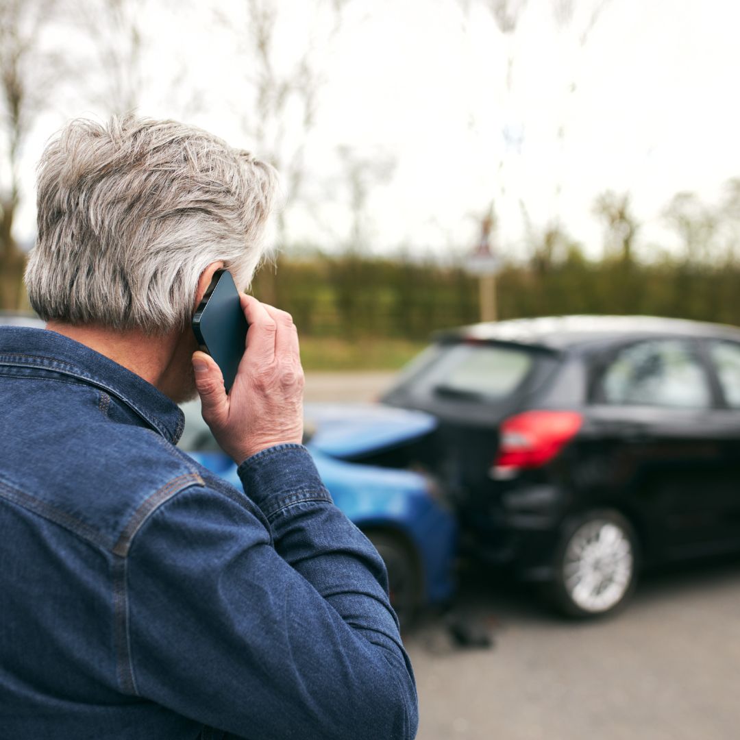 Man on a phone call facing away from the camera and looking at a minor car accident