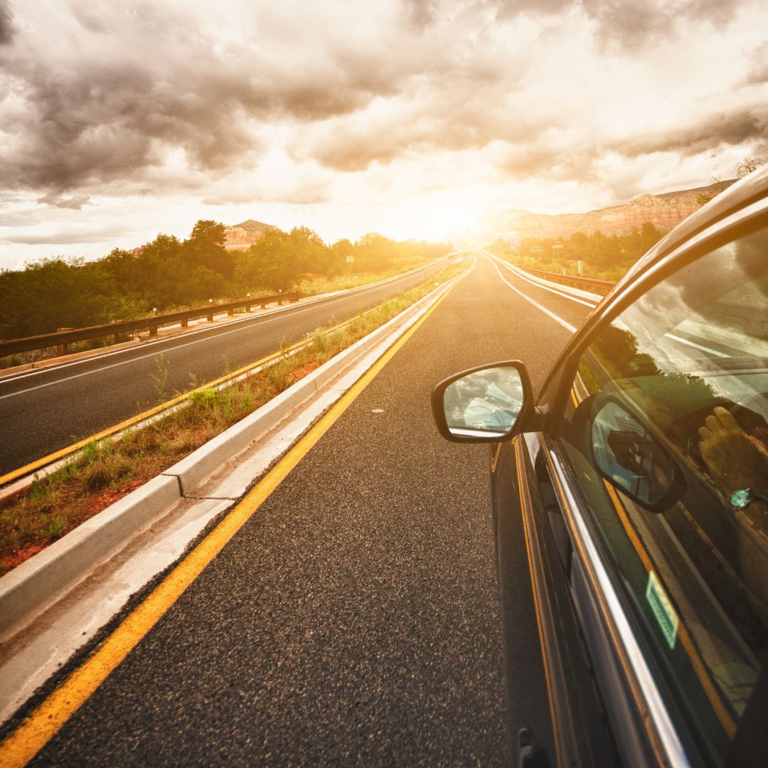A car driving down the highway into a sunset