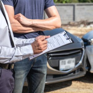 person writing on clipboard in front of car accident